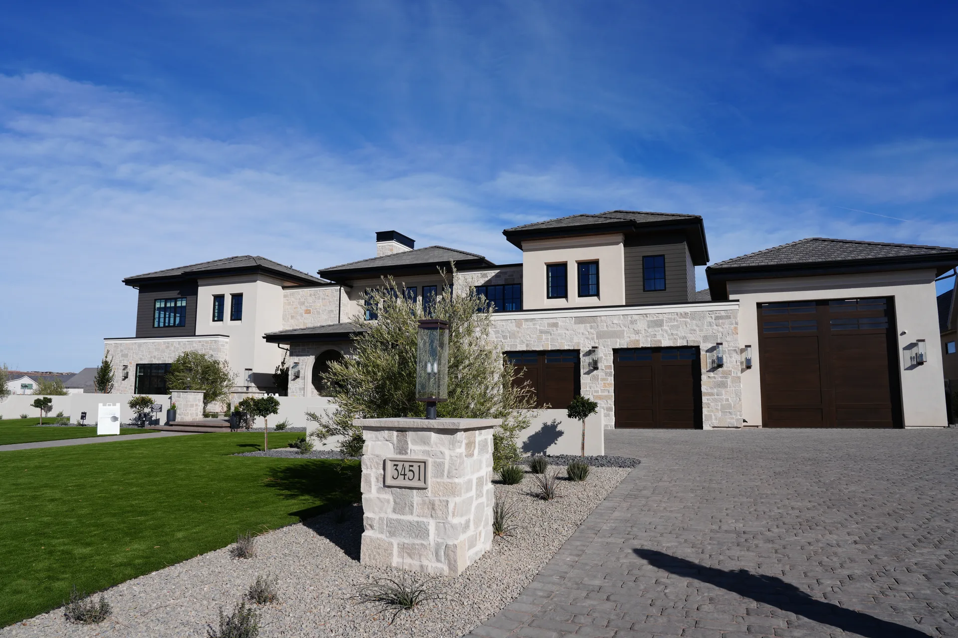 Phoenix custom home front exterior with pale stone, deep roof overhangs, dark wood garage doors, and desert landscaping