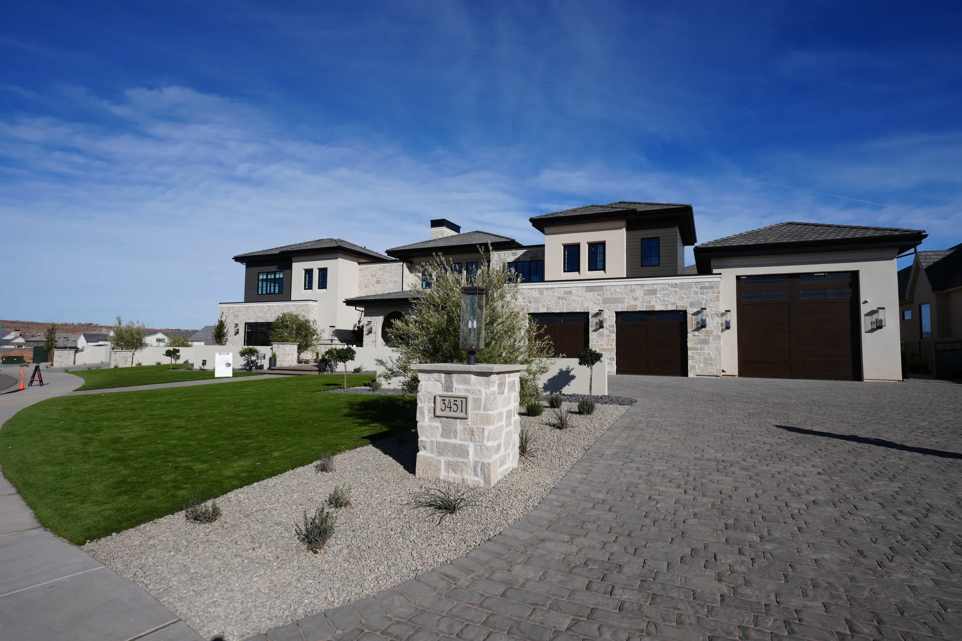 Wide front view of the Phoenix residence with stone facade, paver driveway, lawn, and drought-tolerant planting