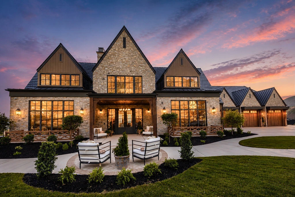 Sunset Haven front exterior at sunset with illuminated windows, steep stone gables, and landscaped entry court